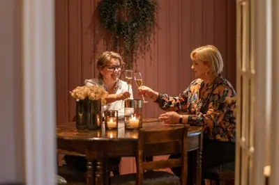two women sitting at a table with glasses of wine at Lampeland Hotel in Lampeland