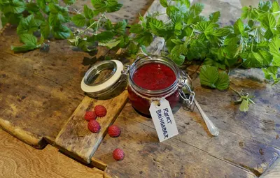 a jar of raspberry jam on a wooden table with raspberries at Lampeland Hotel in Lampeland