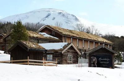 a log cabin with a snow covered mountain in the background at Bjerkeløkkja Bed and Breakfast in Oppdal