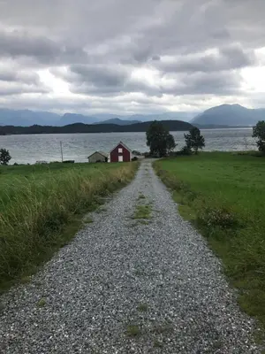 a gravel road leading to a red house next to a lake at Nicoll-huset in Ølve