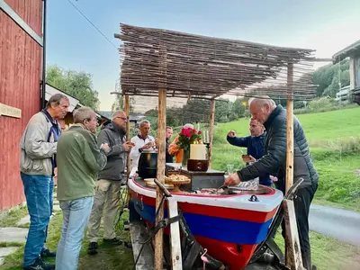 a group of people standing around a boat with a man preparing food at Hesla Farm in Gol
