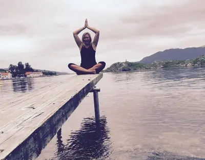 a woman doing a yoga pose on a dock in the water at Skånevik Fjordhotel in Skånevik