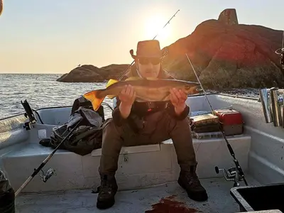a man in a hat sitting on a boat holding a fish at 8 person holiday home in averøy in Henda