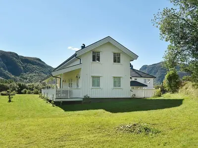 a white house in a field with mountains in the background at 8 person holiday home in Oksvoll in Oksvoll