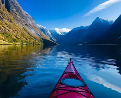 a red kayak on a body of water with mountains at Kjøsnes Feriehytter in Skei