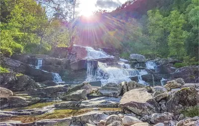 a waterfall on a rocky hill with the sun shining at Three-Bedroom Holiday Home In Vikanes in Eiknes