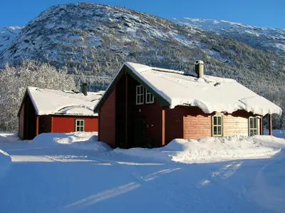 a house covered in snow with a mountain in the background at Jostedal Camping in Jostedal