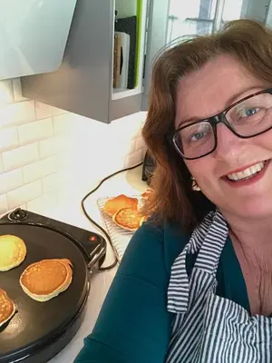 a woman in glasses is smiling next to pancakes at Fjord View Apartment in Stranda