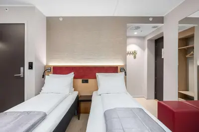 a room with two beds and a red chair at Bergen Harbour Hotel, WorldHotels Crafted in Bergen