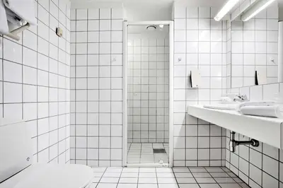 a white tiled bathroom with a shower and a toilet at Best Western Plus Hotel Bakeriet in Trondheim