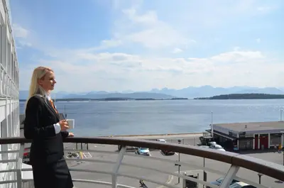 a woman standing on a balcony with a cup in her hand at Thon Hotel Moldefjord in Molde