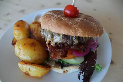 a sandwich on a plate with potatoes and a cherry on top at Vikingskipet Hotell in Hamar