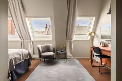 a bedroom with two chairs and a desk and two windows at Home Hotel Bryggen in Bergen