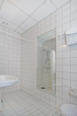 a white tiled bathroom with a shower and a sink at Chesterfield Hotel in Trondheim