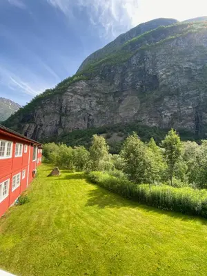 a green yard with a red building and a mountain at Trædal Hotel in Sunndalsøra