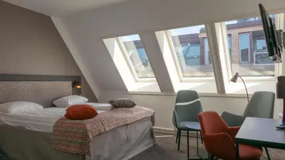 a hotel room with a bed and chairs and windows at Quality Hotel Augustin in Trondheim