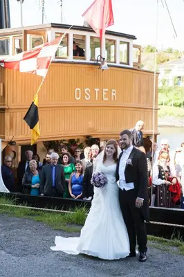 a bride and groom standing in front of a boat at Fjordslottet Hotel in Fotlandsvåg