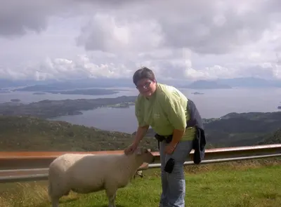 a man is petting a sheep on a hill at Langenuen Motel & Camping in Stord