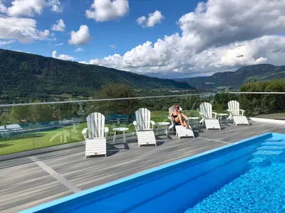 a woman sitting on a deck next to a swimming pool at Nermo Hotel & Apartments in Hafjell