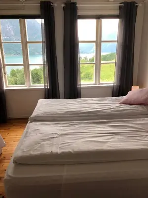 a bed in a bedroom with two large windows at Tunold Gård - Gamle huset in Mindresunde