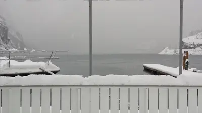 a fence covered in snow next to a body of water at Flåm Marina in Flåm