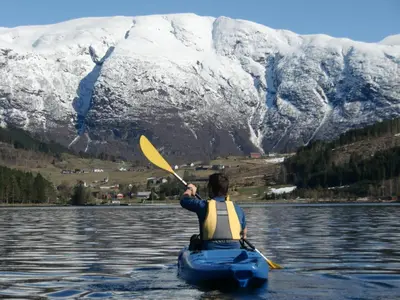 a person in a kayak on a lake with a snow covered mountain at Strand Fjordhotel in Ulvik