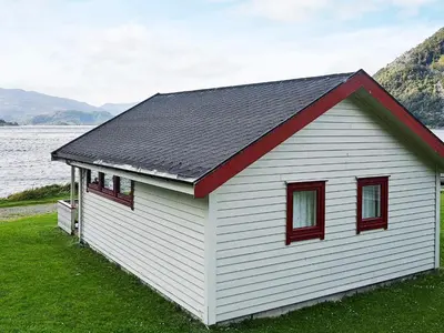 a white building with red windows next to a body of water at 5 person holiday home in Selje-By Traum in Selje