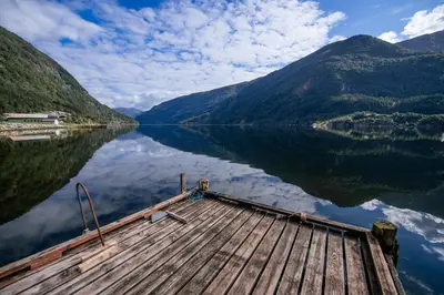 a dock on a lake with mountains in the background at Bazyl Apartment in Folkedal
