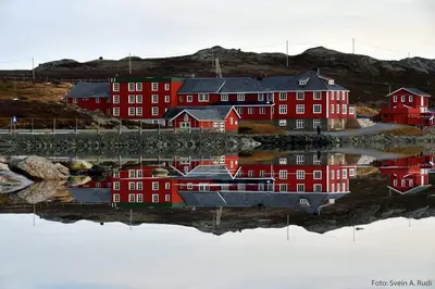 a reflection of red buildings in a body of water at Bygdin Høyfjellshotell in Beitostøl