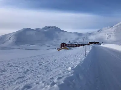 a snow covered road with houses and mountains in the background at Bygdin Høyfjellshotell in Beitostøl
