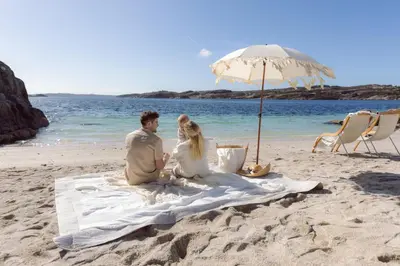 a man and woman sitting on a blanket on the beach at Panorama Hotell & Resort in Steinsland
