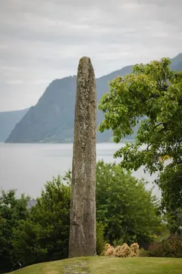 a tall stoneolith on top of a field with a lake at Leikanger Fjordhotel - Unike Hoteller in Leikanger