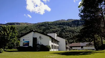 a white building with a mountain in the background at Nordfjord Hotell in Nordfjordeid