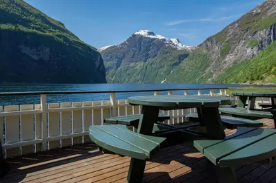 a deck with picnic tables and a view of a mountain at Grande Hytteutleige og Camping in Geiranger