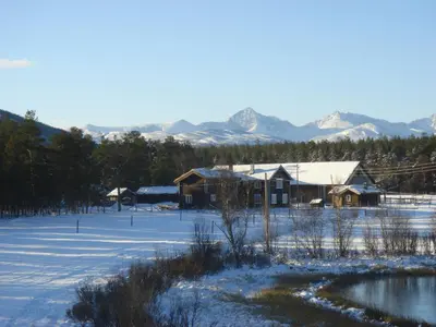 a house in a snowy field with mountains in the background at Kvebergsøya Gard in Grimsbu