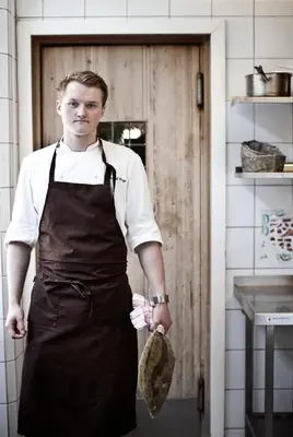 a man wearing an apron standing in a kitchen at Fossheim Hotel Lom in Lom
