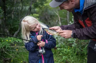 a little girl is holding a fish in her hand at Gomobu Fjellstue in Ron