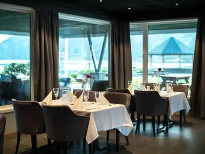 a dining room with tables and chairs and windows at Bremanger Fjord Hotell in Svelgen