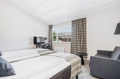 a bedroom with two beds and a chair and a window at Frich's Hotell og Spiseri Alvdal in Alvdal