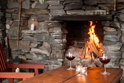 two glasses of wine sitting on a wooden table in front of a fireplace at Bodvarstova in Stryn