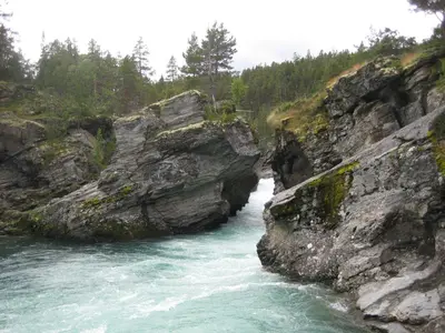 a river flowing through a rocky canyon with trees at Jotunheimen Feriesenter in Heidal