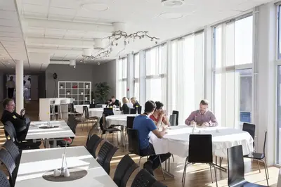 people sitting at tables in a room with large windows at P-Hotels Brattøra in Trondheim