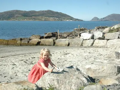 a little girl in a red dress sitting on the beach at 6 person holiday home in Åram-By Traum in Sandvik