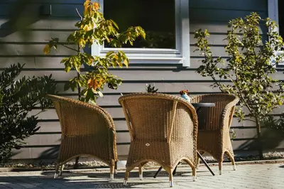 three wicker chairs and a table in front of a house at Solund Leileghetshotell in Hardbakke