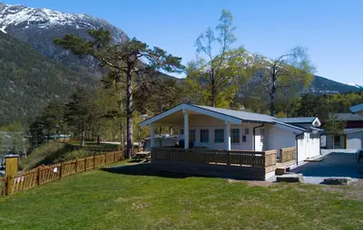 a small white house with a fence and mountains at Kinsarvik Camping in Kinsarvik
