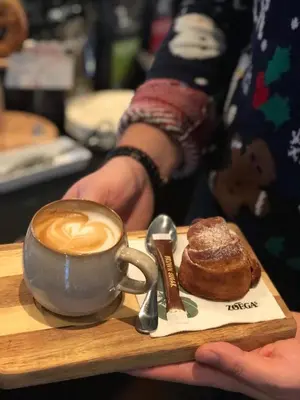 a person holding a tray with a cup of coffee and a pastry at Stryn Kaffebar & Vertshus in Stryn
