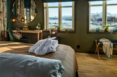 a bedroom with a bed and a table and windows at Knutholmen in Kalvåg