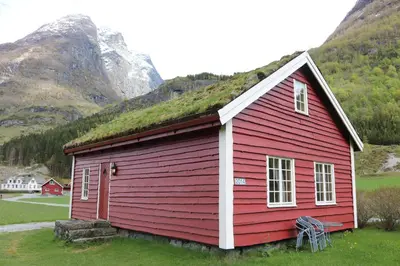 a red house with a grass roof with a mountain at Trollbu Aabrekk gard in Briksdalsbre