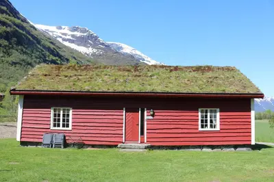 a red house with a grass roof with a mountain at Trollbu Aabrekk gard in Briksdalsbre