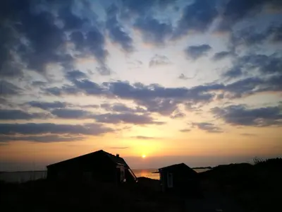 a sunset with the sun setting behind two houses at Kuvågen 23 in Vågenes
